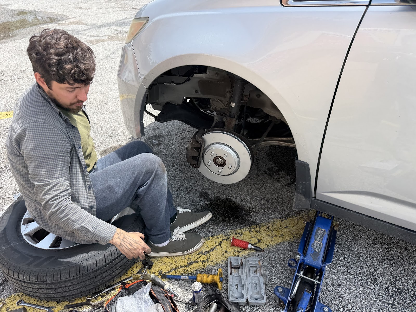 Vinny's mechanic replacing a brake rotor on a car in a Lexington parking lot